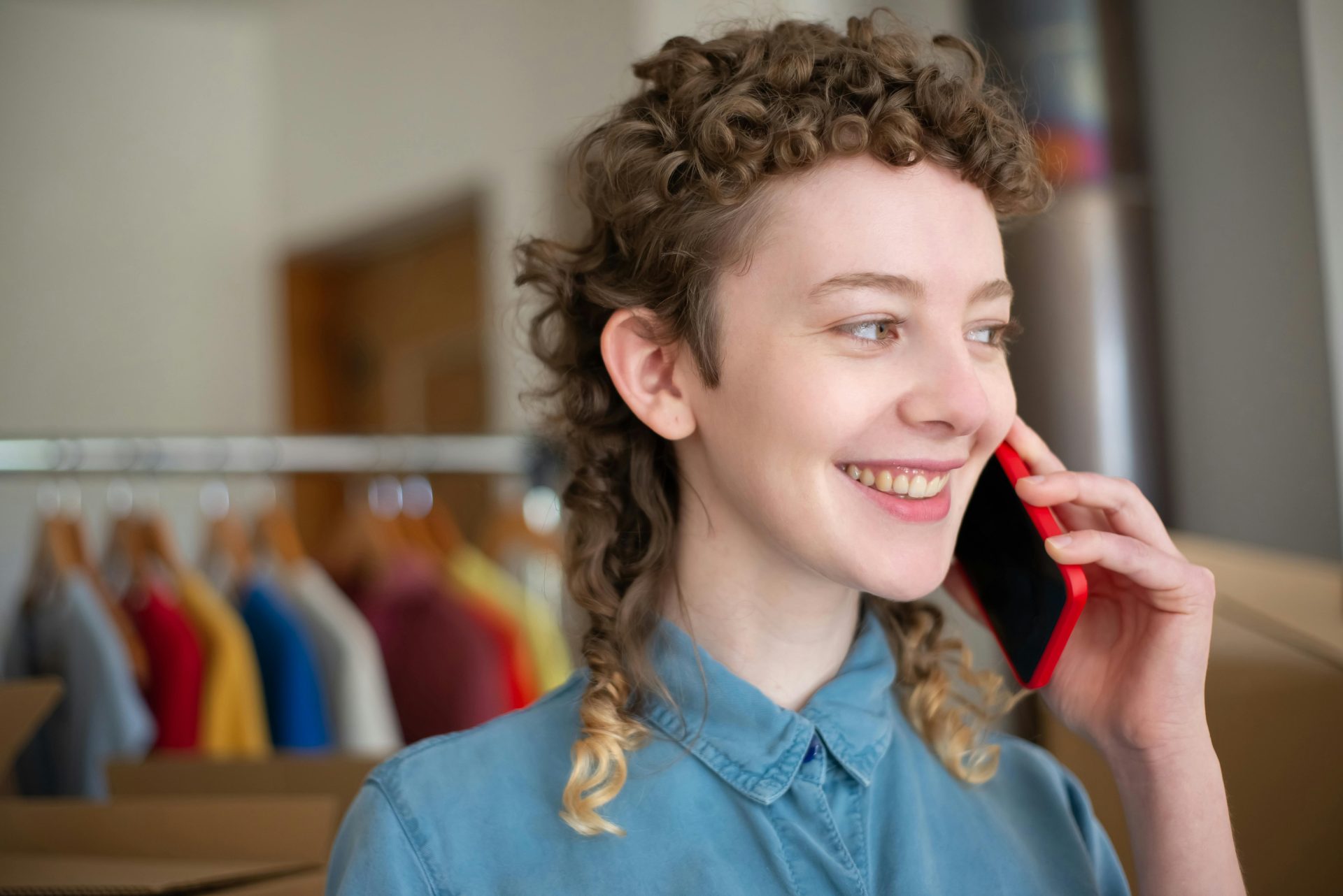 Une femme souriante passe un appel téléphonique dans un intérieur lumineux avec un arrière-plan flou.